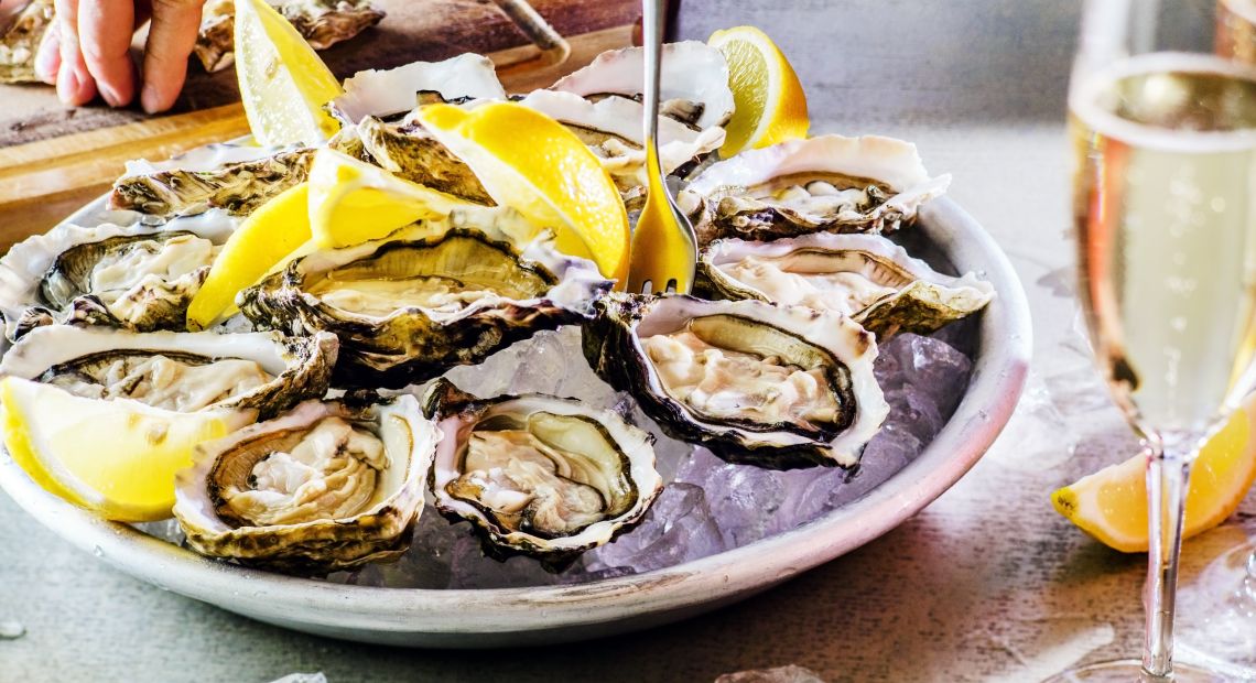 hand on table near plate with oysters served with lemon and glass of sparkling wine