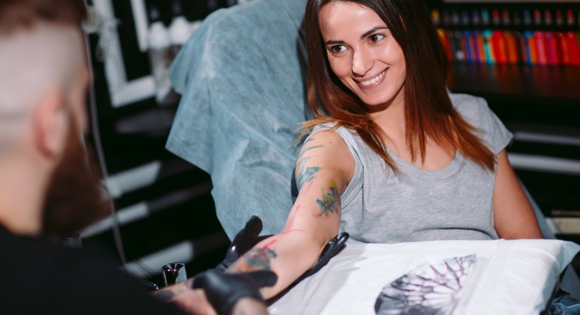 tattoo artist making a tattoo on smiling girl`s hand in salon