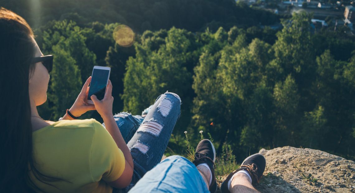 two people sitting on mountain with smart phone