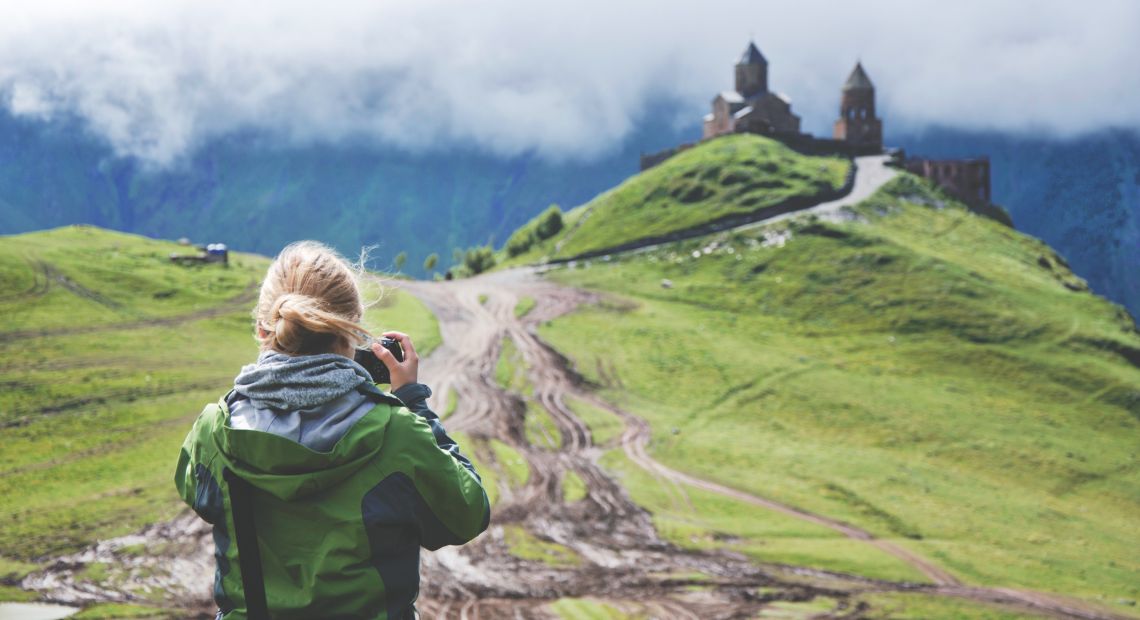 Woman holding camera taking picture of castle on hill