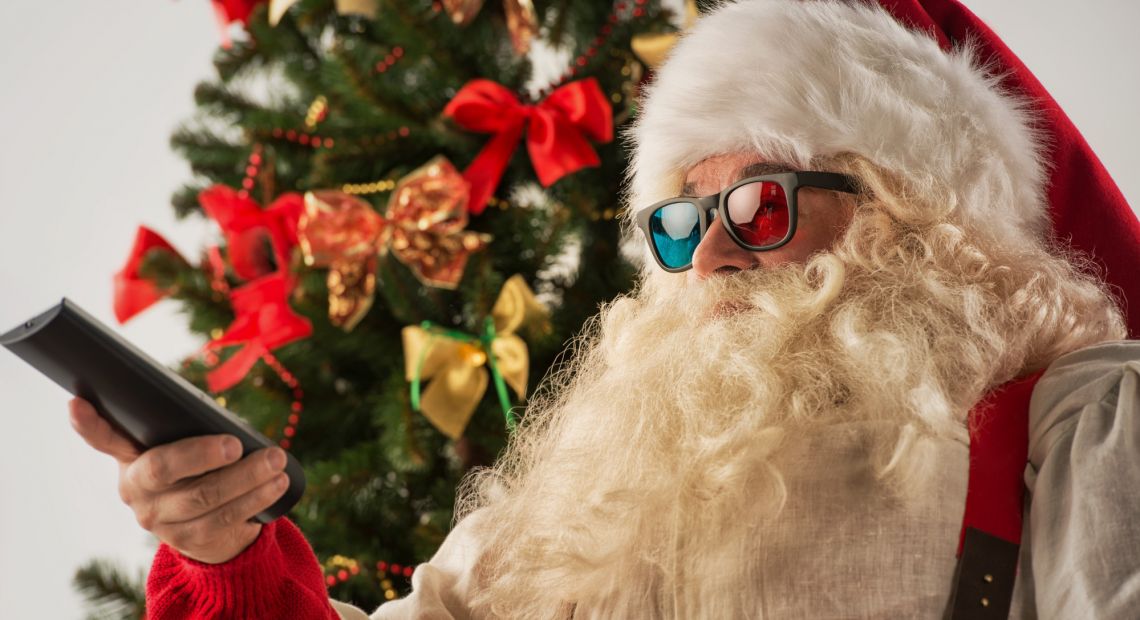 santa claus in colorful glasses with remote near christmas tree