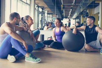 group of people near fitballs having conversation in gym