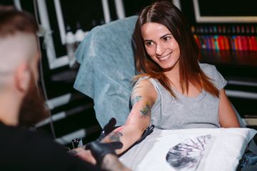 tattoo artist making a tattoo on smiling girl`s hand in salon