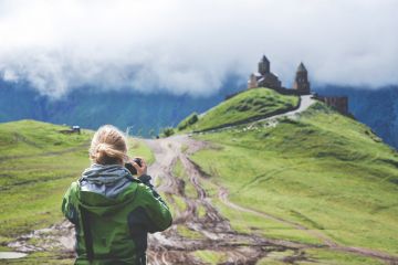 Woman holding camera taking picture of castle on hill
