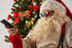 santa claus in colorful glasses with remote near christmas tree