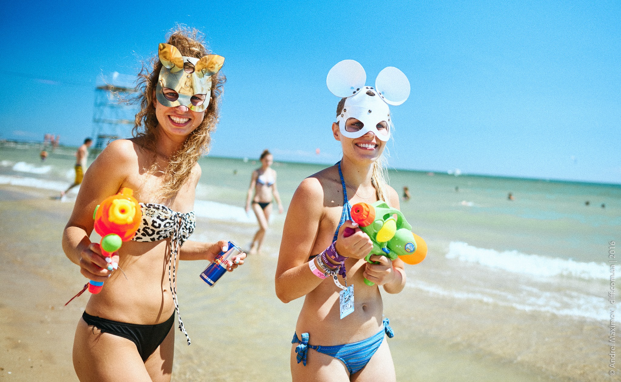 two girls in swimming suits on seashore in masks holding water pistols