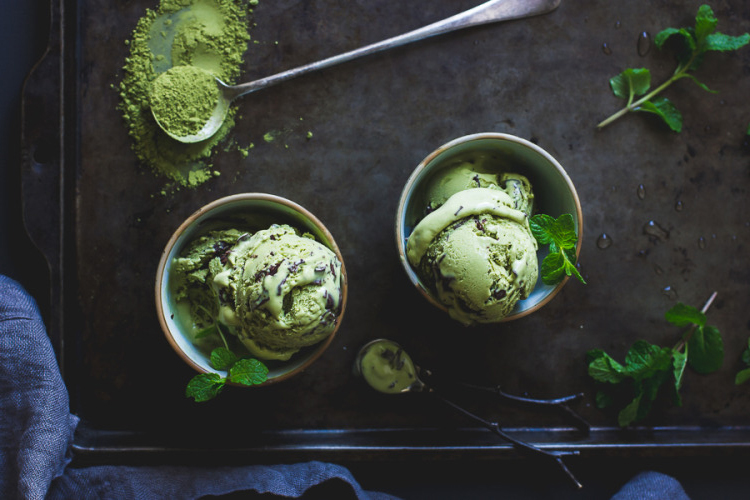 pisctachio ice cream in two cups, spoon and mint leaves