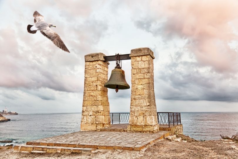 gull flying near ancient bell on the seacoast