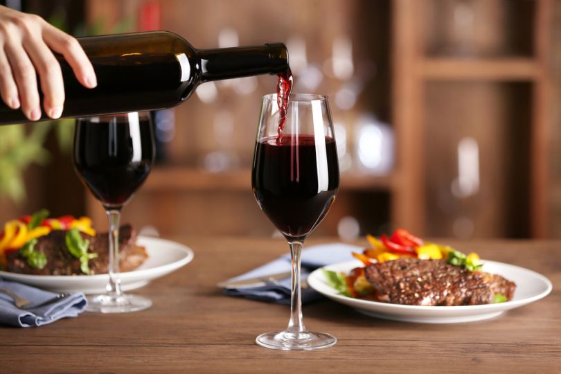 pouring red wine in glasses and served meat dish