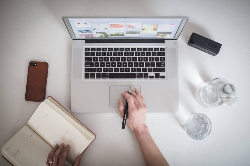 hands with book and pen over laptop