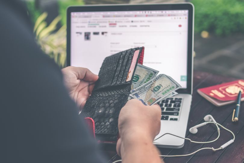 Person holding money in front of a laptop