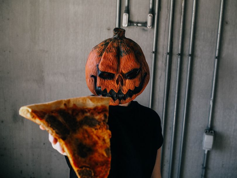 Man with a pumpkin Halloween costume holding a pizza slice