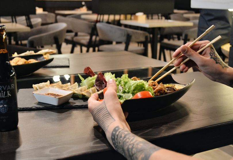 hands holding sticks over dish with asian food