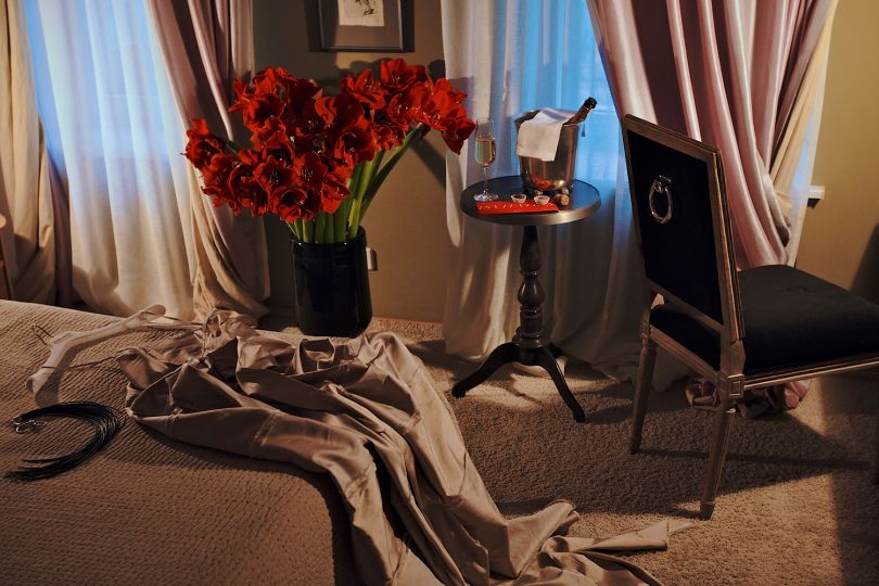 hotel room with classt furniture, glas of wine and vase with red flowers